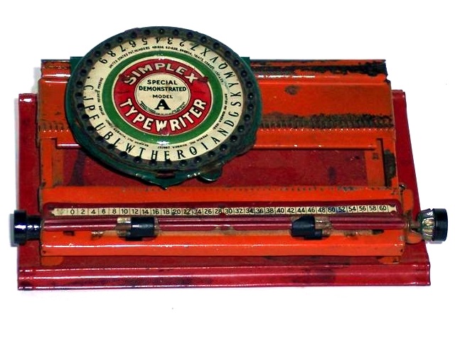 Simplex Special Demonstrated Model A. Small dial with caps and numbers. The metal base is red, the metal body is orange, the paper bail is red with two twirlers and two knobs. The green dial has a bright green inner ring surrounding the logo plate. The logo plate has a red circle with black-edged, large white letters reading Simplex Typewriter. Inside the red circle, against a white background, are the words, Special Demonstrated Model A. The type is sans serif but for the A, which is large, bold, and serif.